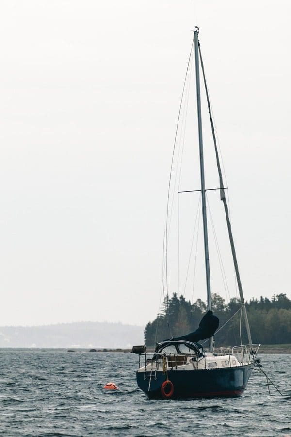 A sail boat with its sail down rests in the water off-shore from Nova Scotia.