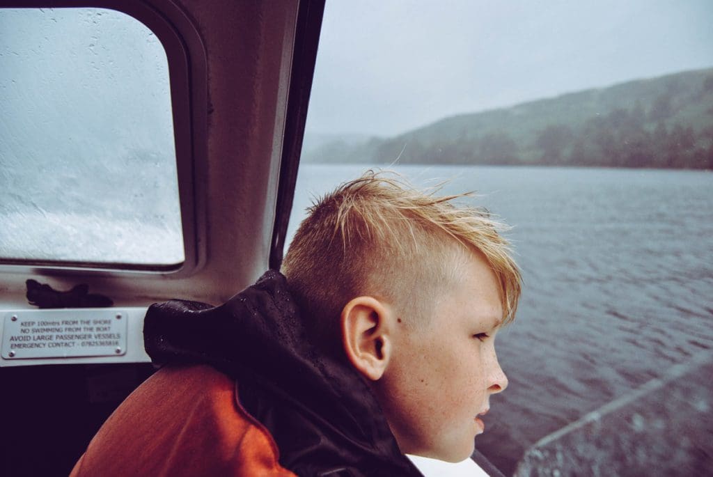 A young boy looks over the edge of a sailing boat into misty waters offshore from Nova Scotia.