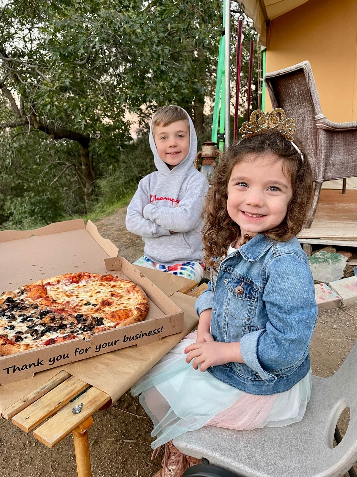 Two kids munch on pizza outside a glamping tent in Julia, CA, one of the best types of accommodations when you visit Julian with kids.