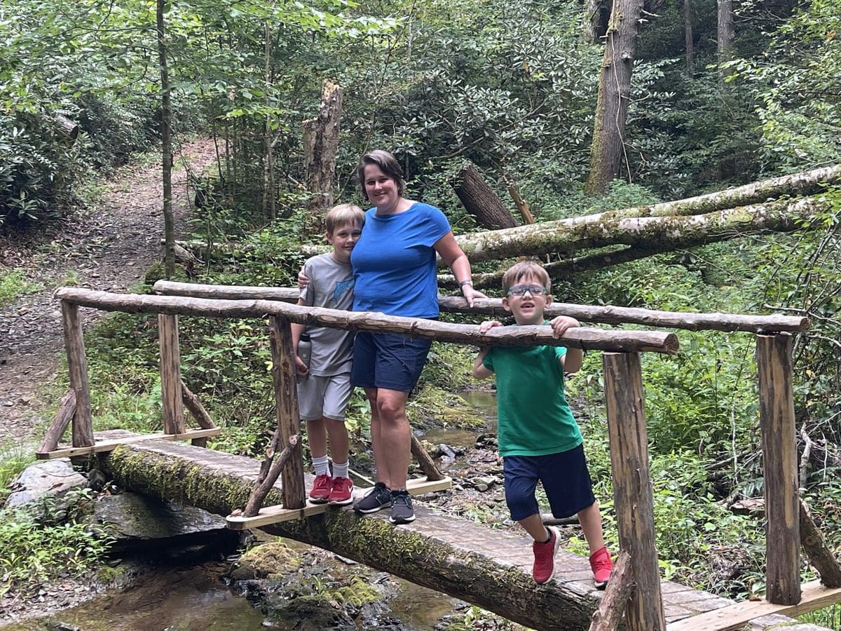 A mom and her two kids stand on a bridge, while hiking at Blackberry Farm.