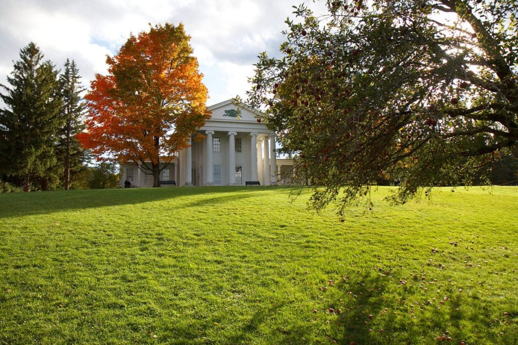 The Shelburne Museum across a grassy field, surrounded by fall foliage on a sunny autumn day in Shelburne.