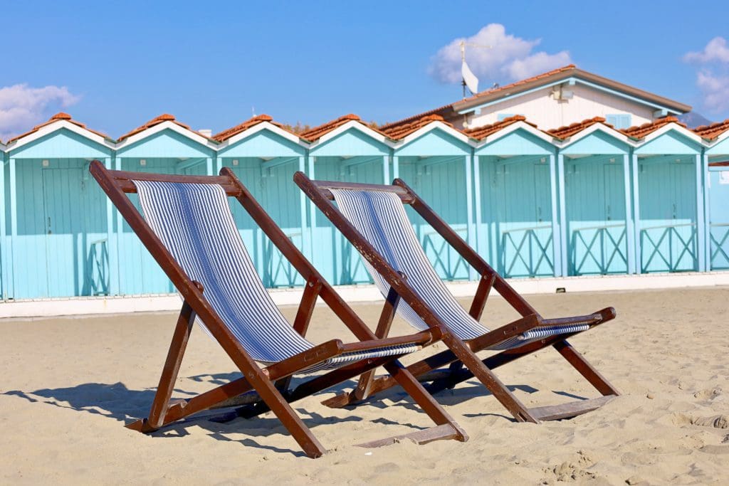 Two blue-striped beach loungers rest in the sand, with turquoise changing cabanas in the background, at Forte dei Marmi, one of the best places to visit in Italy with kids.
