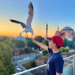A seagull flies down to take a french fry from the hand of a young boy in Istanbul.
