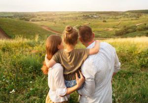 A family of three looks over a beautiful green, grassy scene together.